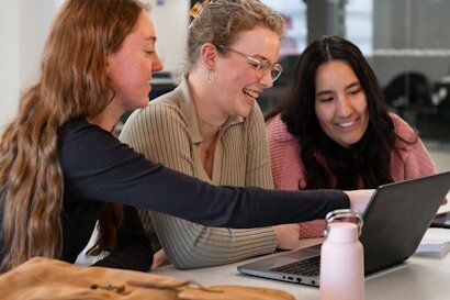 3 Personen, die vor einem Laptop sitzen und miteinander lachen