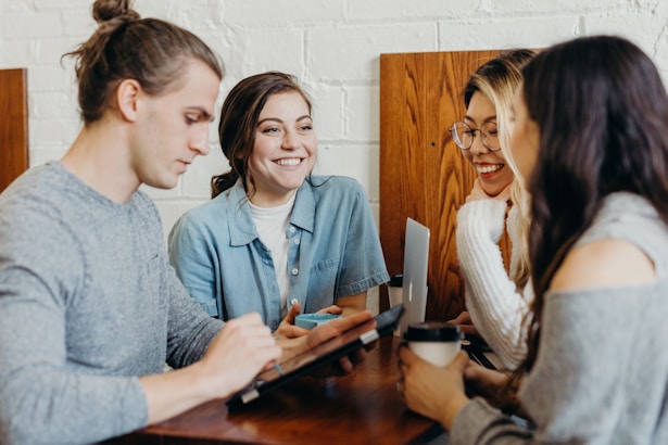 4 Personen, die an einem Besprechungsraum-Tisch stehen und miteinander sprechen